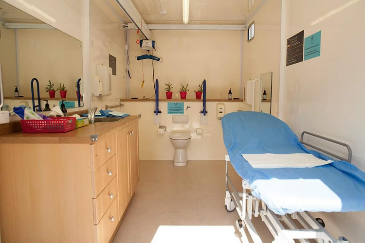 Image of interior of portable wheelchair accessible bathroom with toilet, hoist, adult sized change table and full vanity and separate basin. 