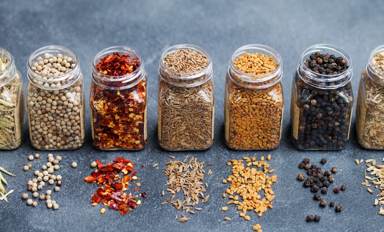 Glass jars with herbs like chilli, fennel seeds, pepper, on a grey background