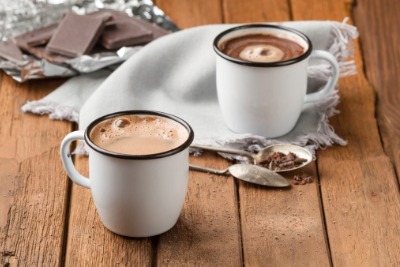 Two mugs of hot chocolate, two spoons and a napkin with pieces of chocolate in the background