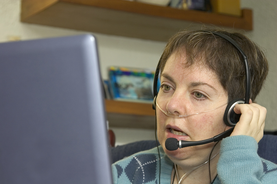 A woman with oxygen tubes and headset looking at a computer.