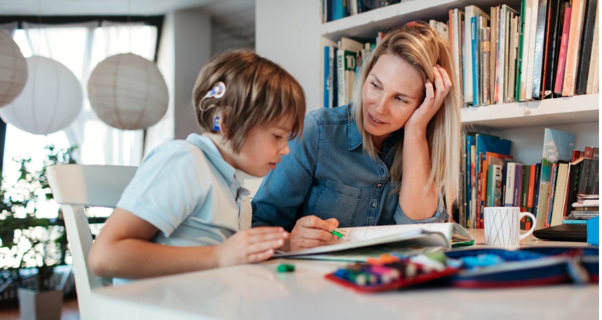Child with cochlear implant sitting alongside an adult, learning
