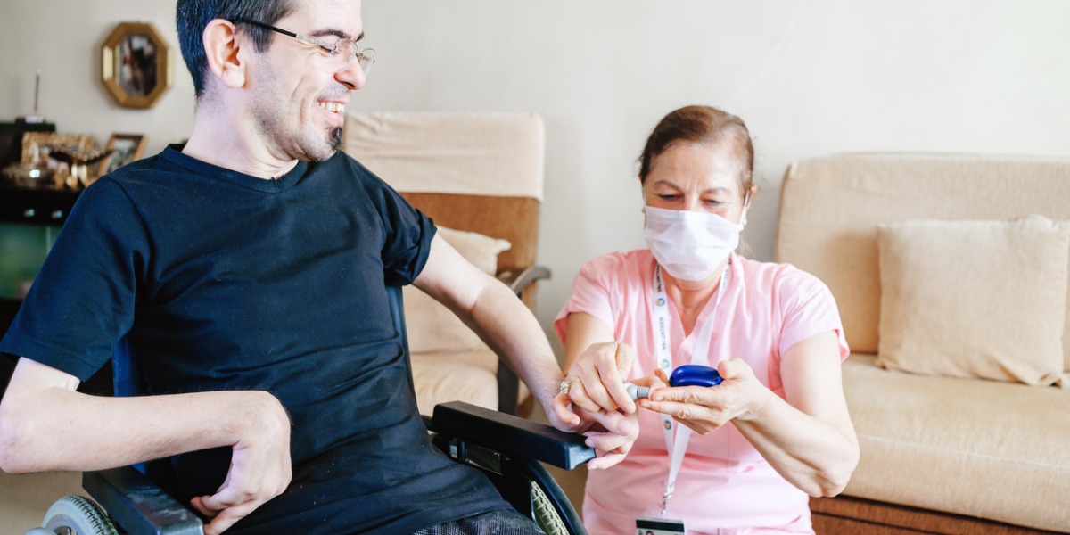 A young man in a wheelchair and a care worker, the careworker is wearing a face mask.