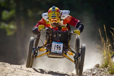 Image of person with disability riding an adaptive mountain bike fast down a dirt trail.