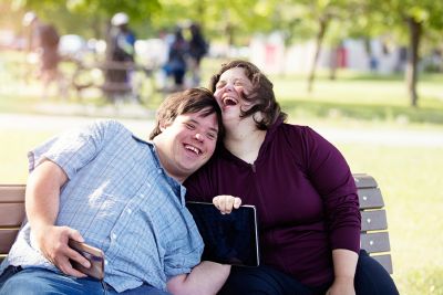 two people with disability sitting on a park bench cuddling