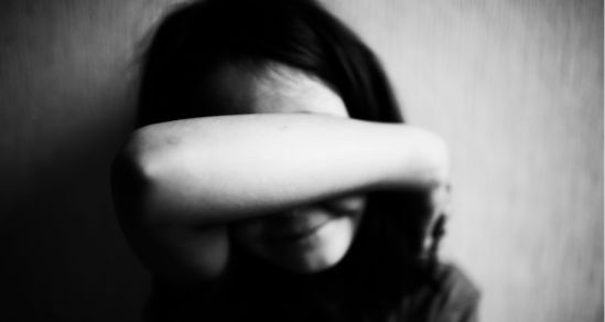 The image in black and white, is of a young girl, who covers her face with her arms, Concept photo of family violence.