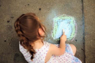 An image of a young girl drawing with chalk on concrete