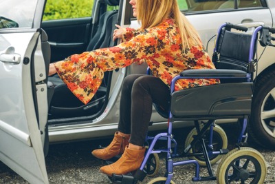 Young woman in a wheelchair getting in a car