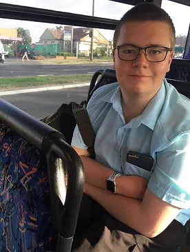 A boy with a blue shirt, wearing glasses, sitting on a bus.